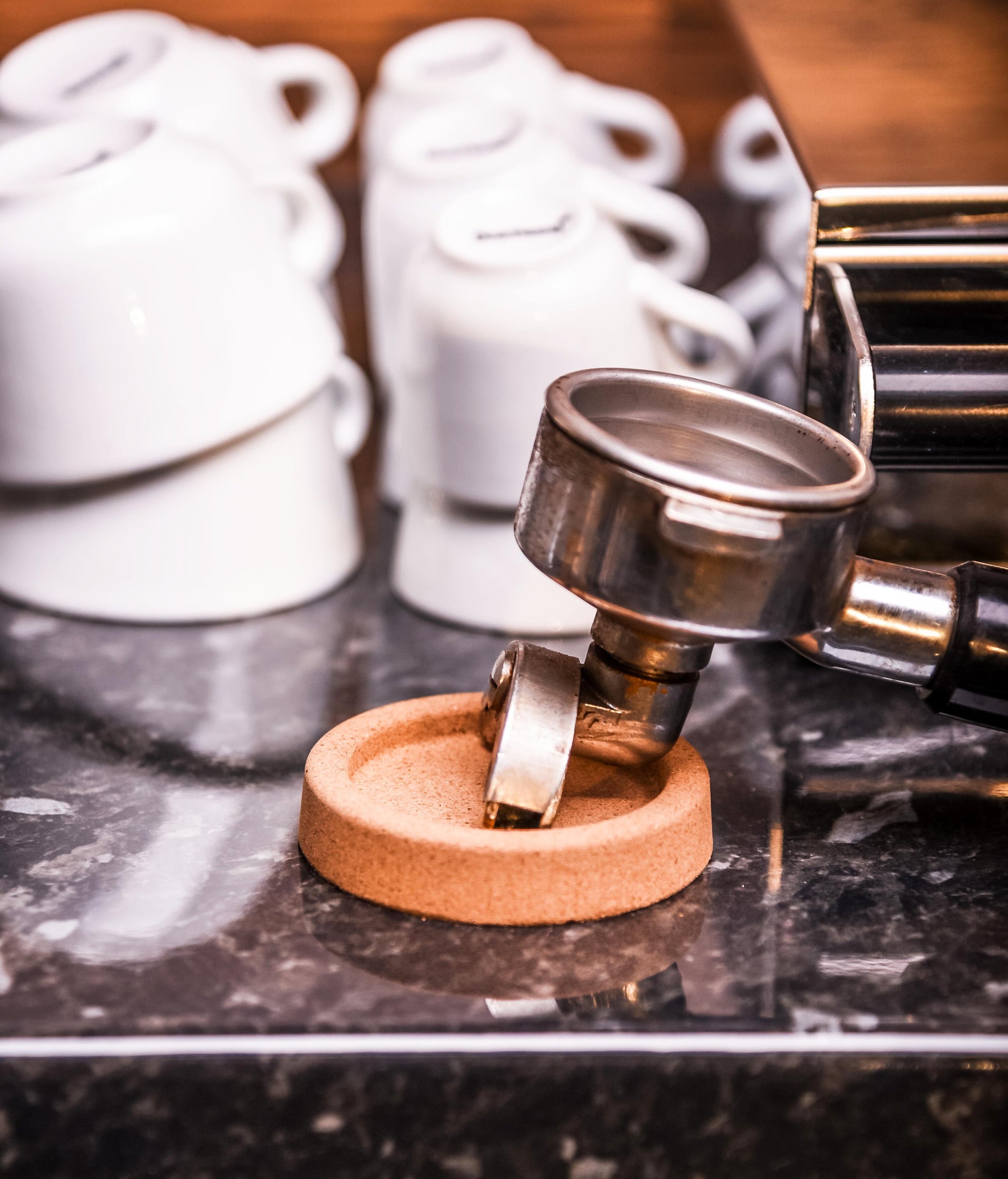 tamper rest with portafilter in front of cappuccino cups and a espresso ma