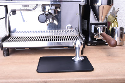 Espresso tamper in front of the espresso machine with barista tools next to it like portafilter tamper mat, Milkpitcher 